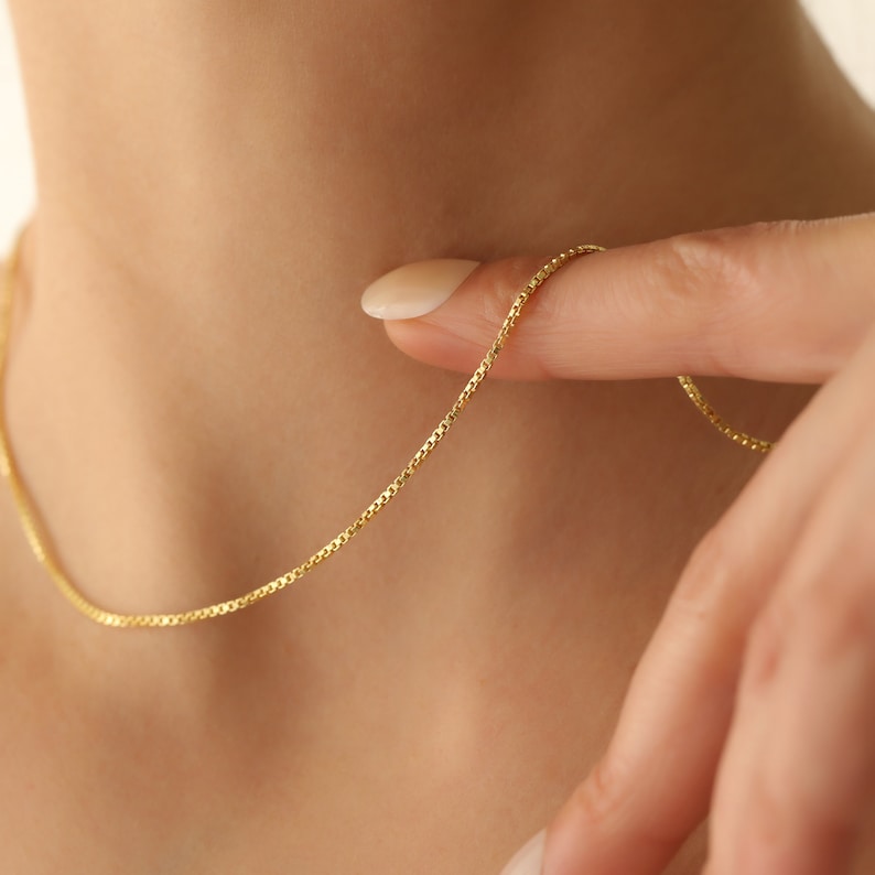 May include: A delicate gold chain necklace with a box chain design. The chain is thin and has a subtle shine.