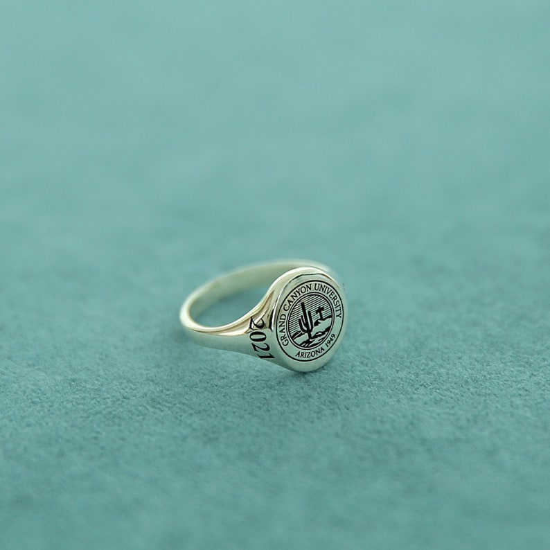 May include: A silver class ring with a raised circular seal featuring the Grand Canyon University logo and the text "Grand Canyon University Arizona 1949". The year "2021" is engraved on the band.
