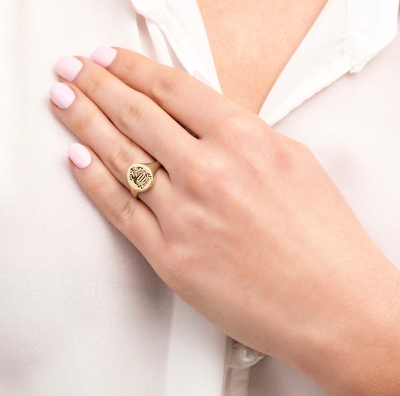 May include: A gold signet ring with an oval-shaped top featuring a detailed engraved design.