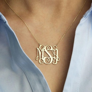 May include: A gold necklace with a large monogram pendant featuring the letters "MSI" in a script font.