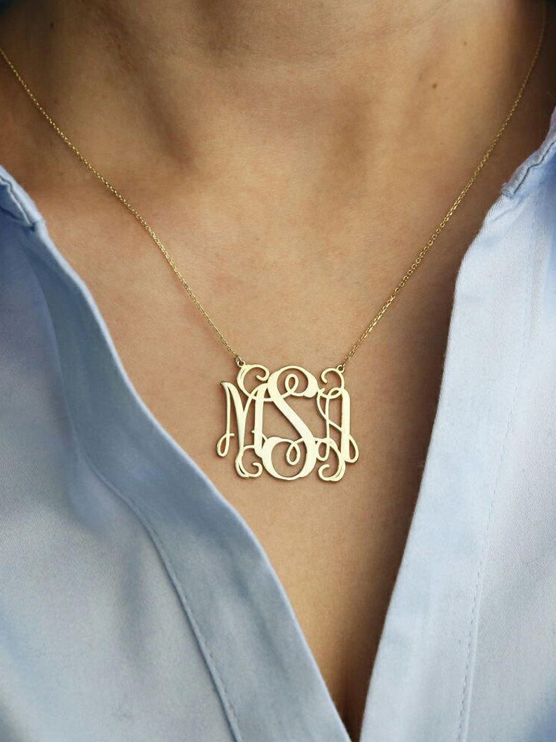 May include: A gold necklace with a large monogram pendant featuring the letters "MSI" in a script font.