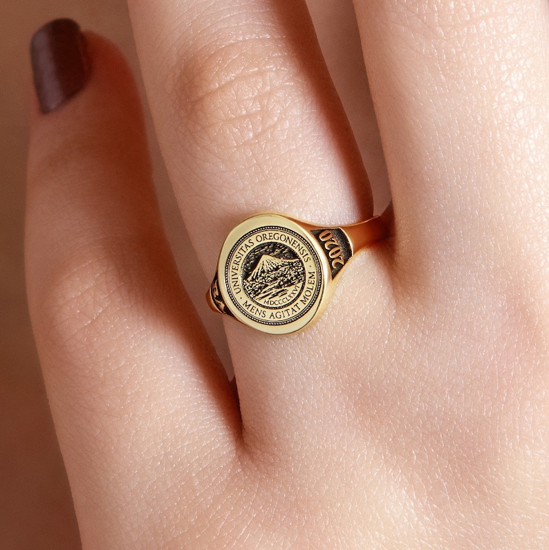 May include: A gold ring with a round, black and gold seal featuring the University of Oregon logo and the text "Universitas Oregonensis - Mens Agitat Molem - MDCCCLXXXIX - 020C".