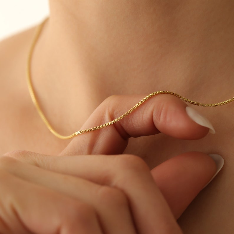 May include: A delicate gold chain necklace with a box chain design. The chain is thin and has a subtle shine.