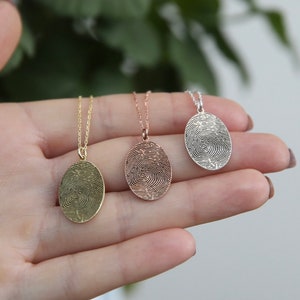 K&ouml;nnte beinhalten: Drei ovale Halsketten mit Fingerabdruck-Anh&auml;ngern. Die Anh&auml;nger sind aus Silber, Ros&eacute;gold und Gold.