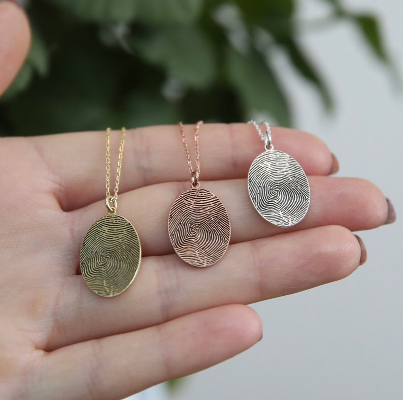 K&ouml;nnte beinhalten: Drei ovale Halsketten mit Fingerabdruck-Anh&auml;ngern. Die Anh&auml;nger sind aus Silber, Ros&eacute;gold und Gold.