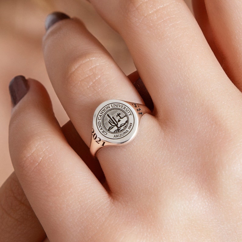 May include: A silver signet ring with a black engraved design of the Grand Canyon University logo. The ring is inscribed with "Grand Canyon University" and "Arizona 1969". The year "2021" is engraved on the side of the ring.