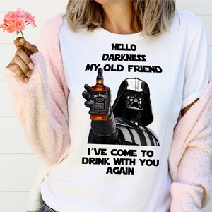 May include: White t-shirt with a black and white image of Darth Vader holding a bottle of Jack Daniel's whiskey. The text "Hello Darkness My Old Friend I've Come To Drink With You Again" is printed on the shirt.