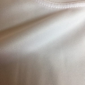 May include: Close-up of a white, textured fabric with a subtle sheen. The fabric has a fine, even weave and a smooth, soft feel.