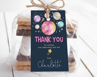 May include: A blue and pink thank you tag with a space theme. The tag features planets, stars, and a rocket ship. The text on the tag reads "Thank you for coming and celebrating with me! Love, Charlotte".