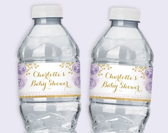 May include: Two clear plastic water bottles with labels that say "Charlotte's Baby Shower" in gold lettering with purple flowers and gold glitter. The labels are printed on a white background.