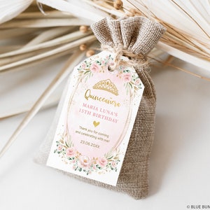 May include: A pink and gold favor tag with a floral design and the text "Quincea&ntilde;era Maria Luna's 15th Birthday" and "Thank you for coming and celebrating with me! 23.06.20XX".