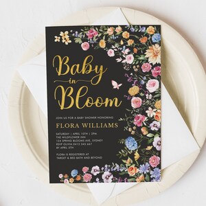 May include: A black baby shower invitation with gold lettering that reads "Baby in Bloom" and floral accents. The invitation includes the name Flora Williams, the date and time of the shower, the location, and RSVP information. It also states that Flora is registered at Target and Bed Bath and Beyond.