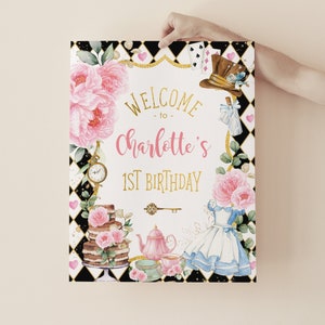 Op de afbeelding: Decoratief bord met de tekst "Welcome to Charlotte's 1st Birthday" in goud en roze. Het bord bevat bloemen en illustraties met het thema Alice in Wonderland, waaronder een taart, theekopjes en een jurk.