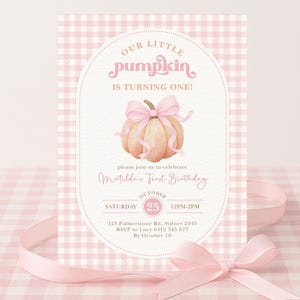May include: A pink and white gingham-patterned invitation card with the text "Our Little Pumpkin is Turning One!" and "Matilda's First Birthday." The card features a watercolour illustration of a pumpkin with a pink bow. A pink ribbon is in the foreground.