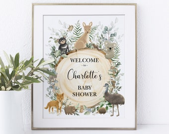 May include: A framed baby shower sign with the text "Welcome to Charlotte's Baby Shower." The sign features illustrations of Australian animals, including a kangaroo, koala, and emu, surrounded by greenery and a wood slice.