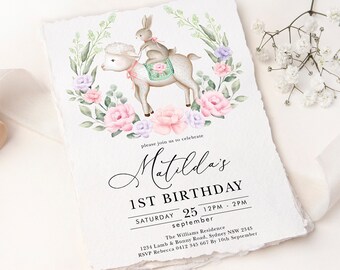 Peut inclure: Une illustration aquarelle d'un agneau blanc avec un lapin qui le chevauche. L'agneau et le lapin sont entourés de fleurs roses et violettes. Le texte "Matilda's 1st Birthday" est écrit en cursive noire. La date "Samedi 25 septembre 12h - 14h" est écrite sous le nom. L'adresse de la résidence Williams et les informations RSVP sont listées sous la date.