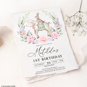 Puede incluir: Una ilustraci&oacute;n de acuarela de un cordero blanco con un conejito montando en su espalda. El cordero y el conejito est&aacute;n rodeados de flores rosas y moradas. El texto "Matilda's 1st Birthday" est&aacute; escrito en letra cursiva negra. La fecha "S&aacute;bado 25 de septiembre 12PM - 2PM" est&aacute; escrita debajo del nombre. La direcci&oacute;n de la residencia Williams y la informaci&oacute;n de RSVP est&aacute;n listadas debajo de la fecha.