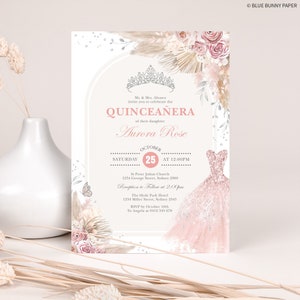 May include: A Quincea&ntilde;era invitation with a pink and silver dress design. The invitation features a floral design with a crown and the text "Quincea&ntilde;era" and "Aurora Rose". The invitation also includes the date, time, and location of the event.