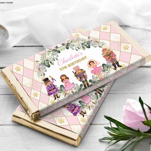 May include: Pink and gold chocolate bar wrappers with a Nutcracker theme. The wrappers feature a green wreath with the text "Charlotte's 5th Birthday".