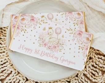 May include: Two pink and gold chocolate bar wrappers with a white swan design and the text "Happy 1st Birthday Georgina".