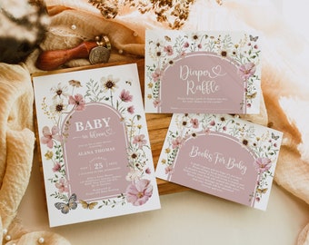 Op de afbeelding: Een set van drie printbare babyshowerkaarten met een bloemenontwerp. De kaarten zijn roze en wit met een bloemenboog en vlinders. De tekst op de kaarten luidt "Baby in Bloom", "Luierspel" en "Boeken voor Baby".