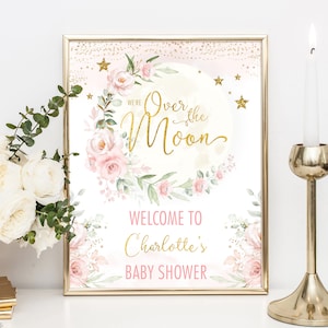 May include: A pink and gold baby shower sign with a watercolour moon and floral wreath. The text reads "We're Over the Moon" and "Welcome to Charlotte's Baby Shower".