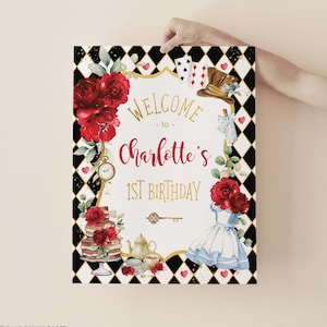 May include: A white welcome sign with black and white checkered background. The sign says "Welcome to Charlotte's 1st Birthday". The sign is decorated with red roses, a teacup, a teapot, a cake, a key, and Alice in Wonderland characters.