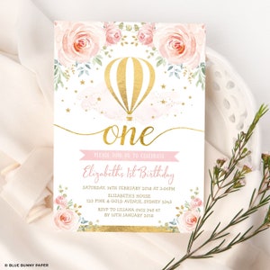 May include: A pink and gold first birthday invitation with a hot air balloon and floral design. The text reads "Please join us to celebrate Elizabeth's 1st Birthday. Saturday, 14th February 2018 at 3:00pm. Elizabeth's House, 123 Pink & Gold Avenue, Sydney 2345. RSVP to Liliana 0412 345 67 by 10th January 2018."