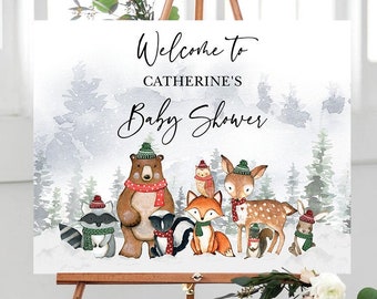 May include: Welcome to Catherine's Baby Shower sign with a winter woodland theme. The sign features a watercolor background with a brown bear, a deer, a fox, a raccoon, a skunk, and an owl. The animals are wearing winter hats and scarves.