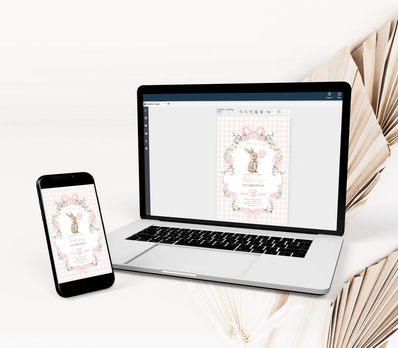 Op de afbeelding: Een laptop en smartphone tonen een digitale uitnodiging met een konijnenillustratie. De uitnodiging heeft een roze ruitjesachtergrond, bloemaccenten en de tekst "1e verjaardag". De apparaten staan op een wit oppervlak.