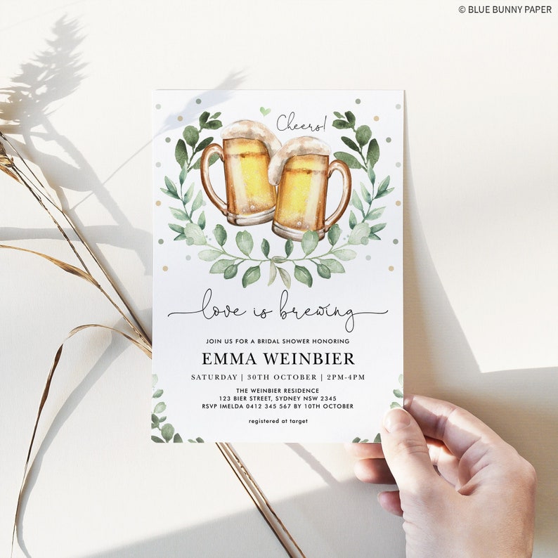 K&ouml;nnte beinhalten: Eine Einladung zu einer Brautparty mit einer Aquarell-Illustration von zwei Bierkr&uuml;gen mit gr&uuml;nen Bl&auml;ttern und dem Text "Cheerol" und "love is brewing". Die Einladung enth&auml;lt den Namen der Braut, Emma Weinbier, das Datum und die Uhrzeit der Party sowie den Ort. Der Text "RSVP Imelda 0412 345 567 by 10th October" und "registered at target" ist ebenfalls enthalten.