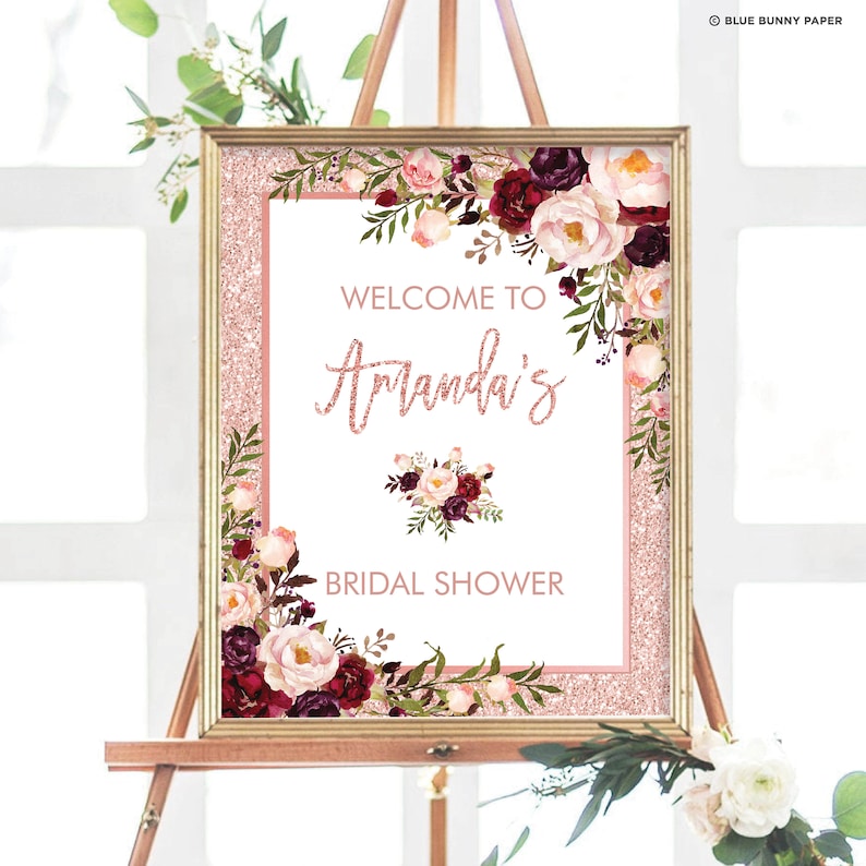 May include: A pink and gold glitter bridal shower welcome sign with burgundy and blush floral accents. The sign reads "Welcome to Amanda's Bridal Shower".