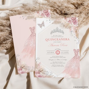 May include: Pink and gold Quincea&ntilde;era invitation with a watercolor illustration of a dress, flowers, and a butterfly. The text reads "Mr. & Mrs. Alvares invite you to celebrate the Quincea&ntilde;era of their daughter Aurora Rose. October 25th at 12:00pm. St. Peter Julian Church, 1234 George Street, Sydney 2000. Reception to follow at 2:00pm. The Hyde Park Hotel, 1234 Miller Street, Sydney 2345. RSVP by October 10th to Angela at 0412 345 678. &copy; BLUE BUNNY PAPER"