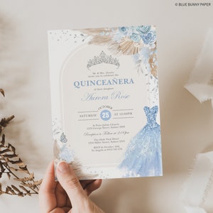 May include: A Quincea&ntilde;era invitation with a blue and white watercolor design. The invitation features a crown, flowers, and a blue dress. The text on the invitation reads "Quincea&ntilde;era" and "Aurora Rose". The date of the event is October 25th.