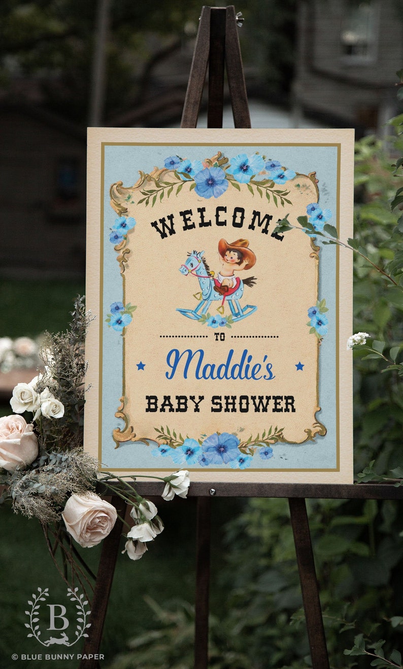 May include: A welcome sign for a baby shower with a blue and white color scheme. The sign features a cartoon baby riding a rocking horse and the text "Welcome to Maddie's Baby Shower".