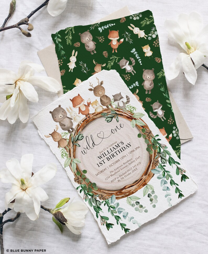 May include: A set of woodland-themed birthday invitations. The main invitation features a wood slice design with the text "wild & one" and event details. A matching green patterned card with woodland animals is also included.