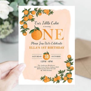 May include: A white invitation card with orange watercolor background and orange illustrations of oranges and green leaves. The text reads "Our Little Cutie is turning ONE. Please Join Us to Celebrate ELLA'S 1ST BIRTHDAY".