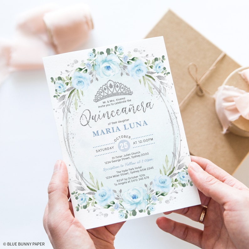 May include: A blue and silver Quincea&ntilde;era invitation with a floral design and a crown. The invitation includes the text "Quincea&ntilde;era" and "Maria Luna" with the date and time of the event.