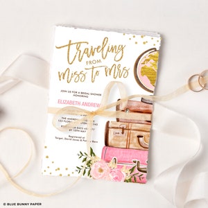 May include: A bridal shower invitation with a watercolor illustration of suitcases and a globe. The invitation is decorated with gold glitter and pink flowers. The text on the invitation reads "Traveling from Miss to Mrs." and includes the bride's name, the date, time, and location of the shower.