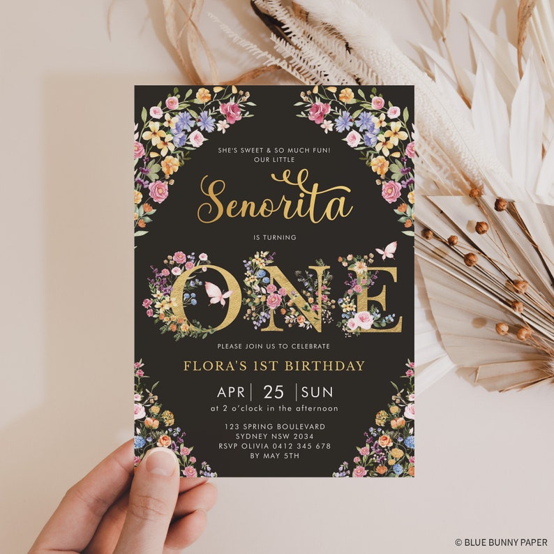 May include: A black and gold floral birthday invitation for a girl's first birthday. The invitation features a gold number one surrounded by flowers and butterflies. The text on the invitation reads "She's sweet & so much fun! Our little Senorita is turning one. Please join us to celebrate Flora's 1st birthday. Apr 25 Sun at 2 o'clock in the afternoon. 123 Spring Boulevard Sydney NSW 2034 RSVP Olivia 0412 345 678 by May 5th. Blue Bunny Paper."