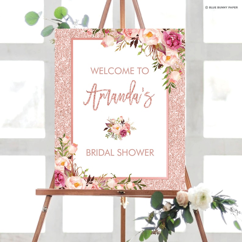 Op de afbeelding: Een roze en wit welkomstschild voor een bruiloft met een glitterachtergrond en bloemmotieven. Het bord staat "Welkom op Amanda's bruiloft".