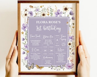May include: A purple and white floral first birthday poster with a photo of a baby girl. The poster includes the baby's name, Flora Rose, her birthdate, weight, height, favorite foods, and favorite song.