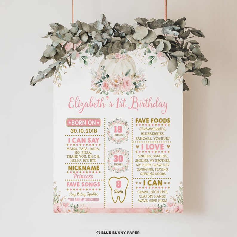 May include: A pink and gold first birthday milestone poster with a pumpkin and floral design. The poster includes details about the child's age, weight, height, and other milestones. The text on the poster reads "Elizabeth's 1st Birthday", "Born on 30.10.2018", "I can say", "Nickname Princess", "Fave Songs", "Fave Foods", "I Love", "I Can", "18 pounds", "30 inches", "8 teeth".