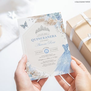 May include: A blue and white quincea&ntilde;era invitation with a watercolor design of a dress, flowers, and butterflies. The invitation includes the text "Quincea&ntilde;era" and "Aurora Rose".
