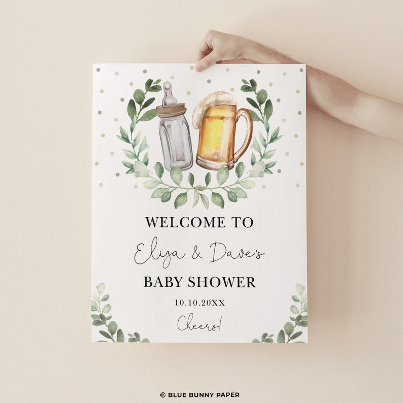 May include: Welcome to Eliza & Dave's Baby Shower sign with a green leafy wreath, a baby bottle, and a beer mug. The date is 10.10.20XX and the text says "Cheers!"