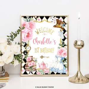 Op de afbeelding: Ingelijste verjaardagsbord met een Alice in Wonderland-thema. Het bord leest "Welcome to Charlotte's 1st Birthday" in goud en roze. Het ontwerp bevat bloemen- en theefeestelementen, een taart en een jurk.