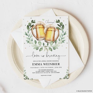 K&ouml;nnte beinhalten: Eine Einladung zu einer Bridal Shower mit einer Aquarell-Illustration von zwei Bierkr&uuml;gen mit gr&uuml;nen Bl&auml;ttern und goldenem Glitzer. Der Text lautet "love is brewing" und enth&auml;lt den Namen der Braut, Emma Weinbier, das Datum und die Uhrzeit der Shower sowie den Ort.