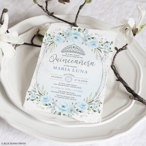 May include: A blue and silver Quincea&ntilde;era invitation with floral accents. The invitation reads "Mr. & Mrs. Alvarez invite you to celebrate the Quincea&ntilde;era of their daughter MARIA LUNA. Saturday, 25 October at 12:00 PM. St. Peter Julian Church, 1234 George Street, Sydney 2000. Reception to follow at 2:00 PM. The Hyde Park Hotel, 1234 Miller Street, Sydney NSW 2345. RSVP by 10th October to Angela at 0412 345 678."