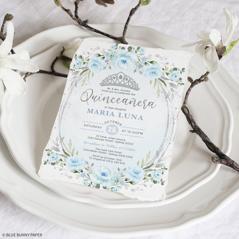 May include: A blue and silver Quincea&ntilde;era invitation with floral accents. The invitation reads "Mr. & Mrs. Alvarez invite you to celebrate the Quincea&ntilde;era of their daughter MARIA LUNA. Saturday, 25 October at 12:00 PM. St. Peter Julian Church, 1234 George Street, Sydney 2000. Reception to follow at 2:00 PM. The Hyde Park Hotel, 1234 Miller Street, Sydney NSW 2345. RSVP by 10th October to Angela at 0412 345 678."