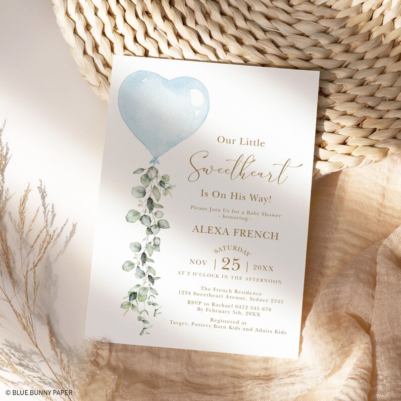 May include: A baby shower invitation with a blue heart-shaped balloon and eucalyptus leaves. The text reads "Our Little Sweetheart Is On His Way!" and includes the date, time, and location of the shower. The invitation is for Alexa French.